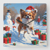 クリスマスの帽子をかぶったパピヨンの犬が雪の中を走る スクエア壁時計 (正面)