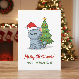 クリスマスツリーの前の赤い帽子をかぶった怒ったグレータビー猫 シーズンカード