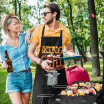 グリルグラフィックのキング エプロン<br><div class="desc">バーベキューと料理の食事に取り憑かれた男がいるのか?彼はグリルの王かもしれない。このおもしろいグラフィックのエプロンで彼の料理のスキルがどれほど高いか彼に知らせなさい。グリルで食事を料理に出ている間に着るのに最適だ。手のレタリングは私のイラストレーションの下に冠をかぶったグリルでメッセージKING OF THE GRILLを綴る。</div>