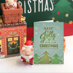 グリーン紙クリスマスツリー シーズンカード<br><div class="desc">紙のクリスマスツリーは緑の色合いで、白で縁取られた。雪片が青い緑の質感の背景に落ちているように見える。緑のタイポグラフィとホリー。</div>