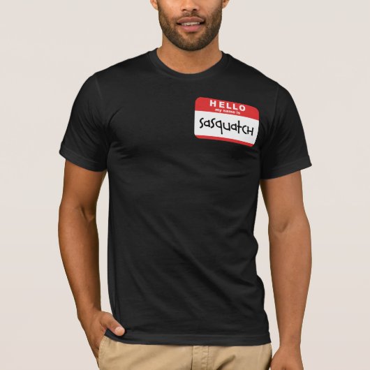 サスカッチの名前入りの記章のTシャツの大きい足のからかい Tシャツ (正面)