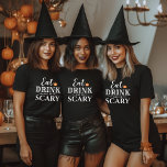 ドリンクと怖い食べタイポグラフィモダンハロウィン Tシャツ<br><div class="desc">オレンジ色のジャックオランタンカボチャのアクセントと文字が付いた白いタイポグラフィのデザインに食べ「ドリンクと怖がる」というフレーズを付け加え、お名前や家族の名前と一緒に楽しめる恐ろしいかわいい女性のグラフィックTシャツでパーソナライズされたす。</div>