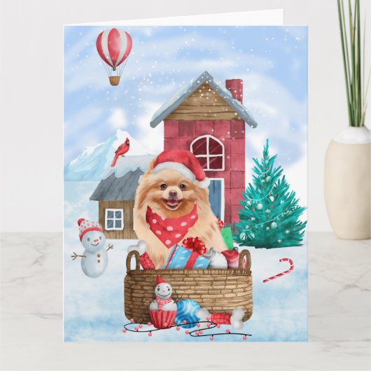 ポメラニアンの犬が雪のそばのクリスマスツリーと犬小屋に座っている カード (正面)