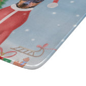 ミニチュア・ピンシュの雪にクリスマスのプレゼントを贈る犬 カッティングボード (角)