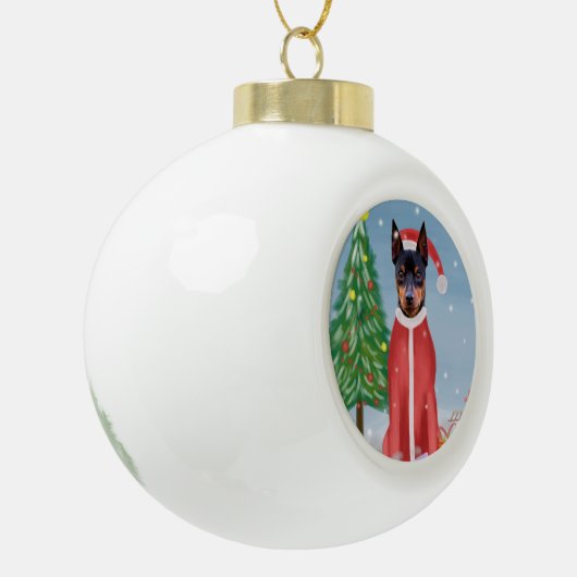 ミニチュア・ピンシュの雪にクリスマスのプレゼントを贈る犬 セラミックボールオーナメント (左)
