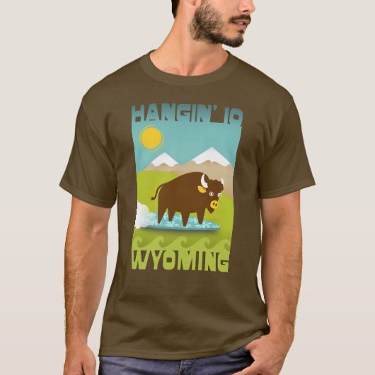 ワイオミング州の山々をバックにバイソンをサーフィンさせる面白Tシャツ Tシャツ (正面)