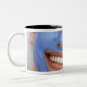 微笑する顔のマスクを身に着けている若い女性 ツートーンマグカップ (左)