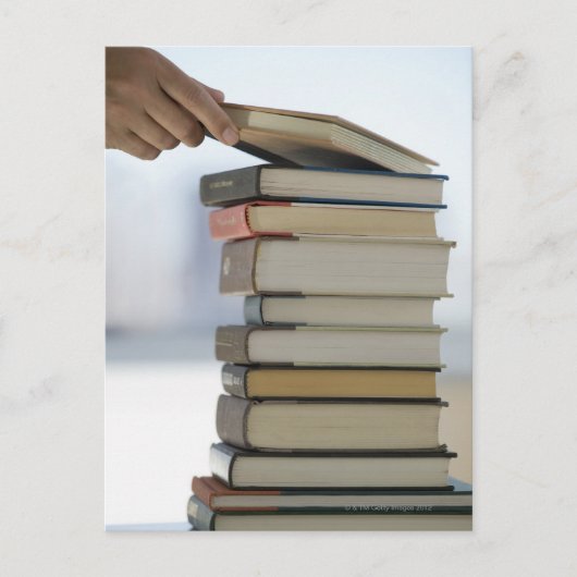 本の積み重ねからの本を取る人の手 ポストカード (正面)