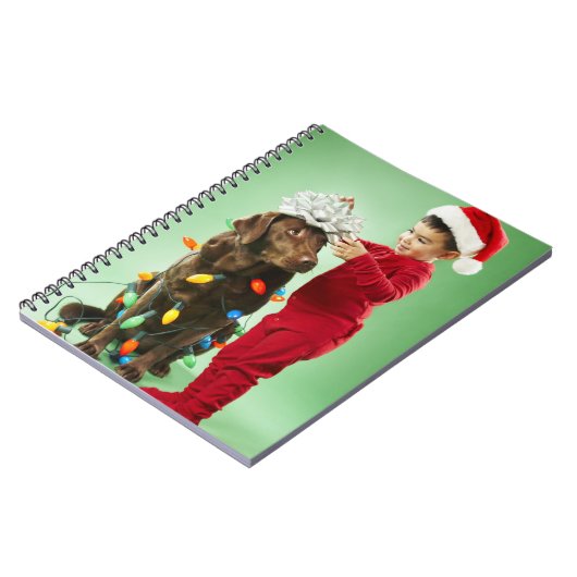 犬のまわりでクリスマスの照明を包んでいる若い男の子 ノートブック (左側)