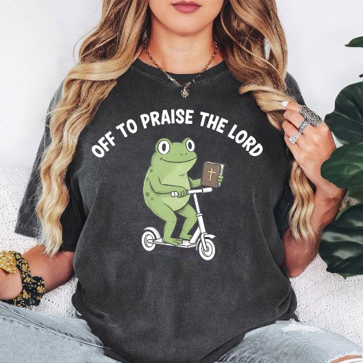 聖書を持ったスクーターに乗るカエルの面白いデザイン Tシャツ