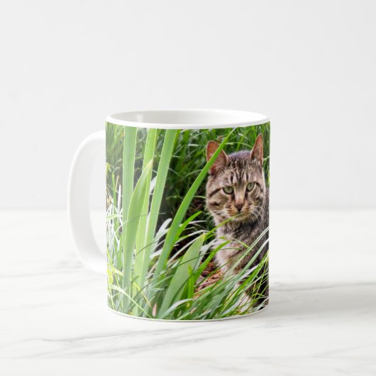 芝生に座るトラ猫の写真 コーヒーマグカップ (正面左)