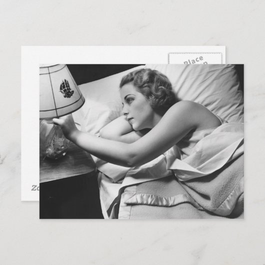 若い女性がベッドに横たわってランプを消している ポストカード (正面/裏面)