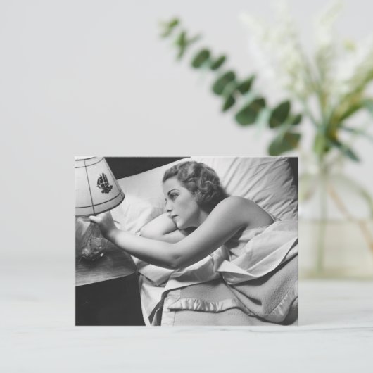 若い女性がベッドに横たわってランプを消している ポストカード (スタンド正面)