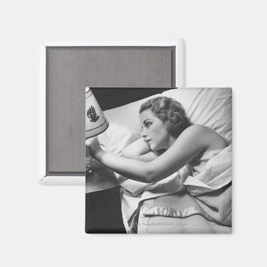 若い女性がベッドに横たわってランプを消している マグネット (正面/裏面)