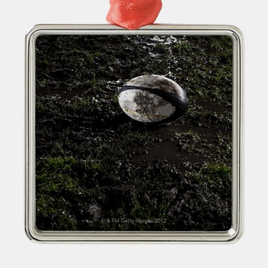 草の上でかみ砕かれるに坐る泥のラグビーのボール メタルオーナメント (正面)