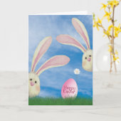 草の中にピンクの卵を持つイースターバニー カード (黄色い花)