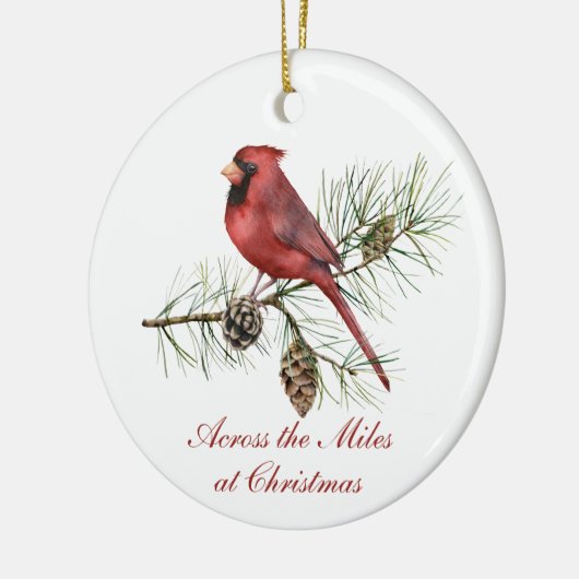 赤い(鳥)ショウジョウコウカンチョウの松のコーンがマイルスのクリスマスを横切る セラミックオーナメント (左)