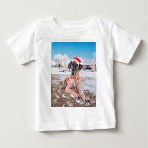 雪に座るグレートデーンの犬 クリスマス帽子 ベビーTシャツ