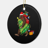 雪のクリスマスツリーの中を歩くビッグフット セラミックオーナメント (左)