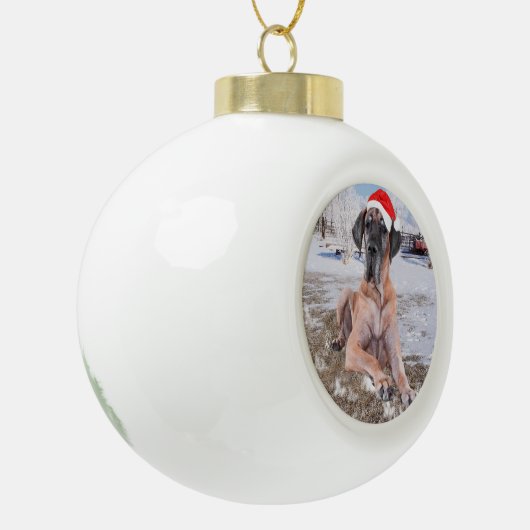 雪のクリスマスハットに座って可愛い大きなデーン犬 セラミックボールオーナメント (左)