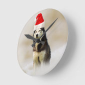 雪の中にサンタハットを持つシベリアのハスキー犬 ラウンド壁時計 (傾斜)