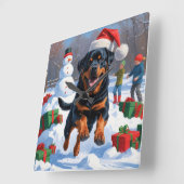 雪の中を走るロットワイラー　クリスマス帽子をかぶって スクエア壁時計 (傾斜)