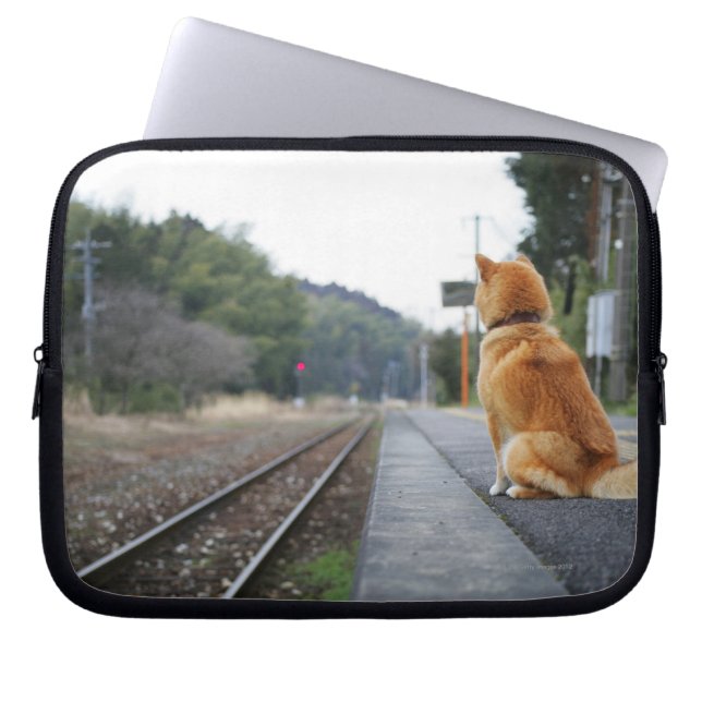 駅に座っている犬 ラップトップスリーブ (正面)
