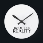 Rooted In Reality Minimalist Typewriter  ラウンド壁時計<br><div class="desc">Own the present moment. This modern wall clock features sharp typewriter numerals and a central message reminding you to stay anchored in the here and now.</div>