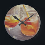 Sangria and Sunshine ラウンド壁時計<br><div class="desc">This image shows a refreshing glass and pitcher of citrus sangria, perfect for a warm day. The fresh slices of lemon and orange add bright colour and hint of natural sweetness. One glass sits ready to enjoy while sangria is being poured from a small glass pitcher beside it, perfect for...</div>