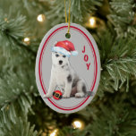 Siberian Husky Santa Hat Christmas Ornament セラミックオーナメント<br><div class="desc">On the front of this Christmas ornament is an image of an adorable Siberian Husky puppy wearing a red and white Santa hat. The puppy has found a Holiday tree bulb that looks like a Santa Claus belt, and is ready to play. Beside him is the text in red "JOY"....</div>