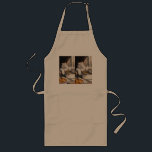 The Gentle Tiger Chef ロングエプロン<br><div class="desc">In a sunlit kitchen that feels both rustic and peaceful, a white tiger has taken on the role of chef. With calm confidence, the striped cook leans over a simmering pot, carefully stirring a hearty golden stew. Steam rises in soft curls while a plate of crisp, golden food rests nearby,...</div>